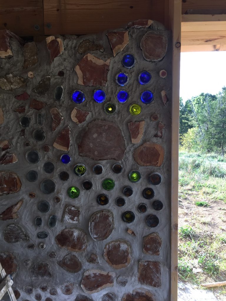 A little blue truck made out of bottles inside of a cordwood wall 